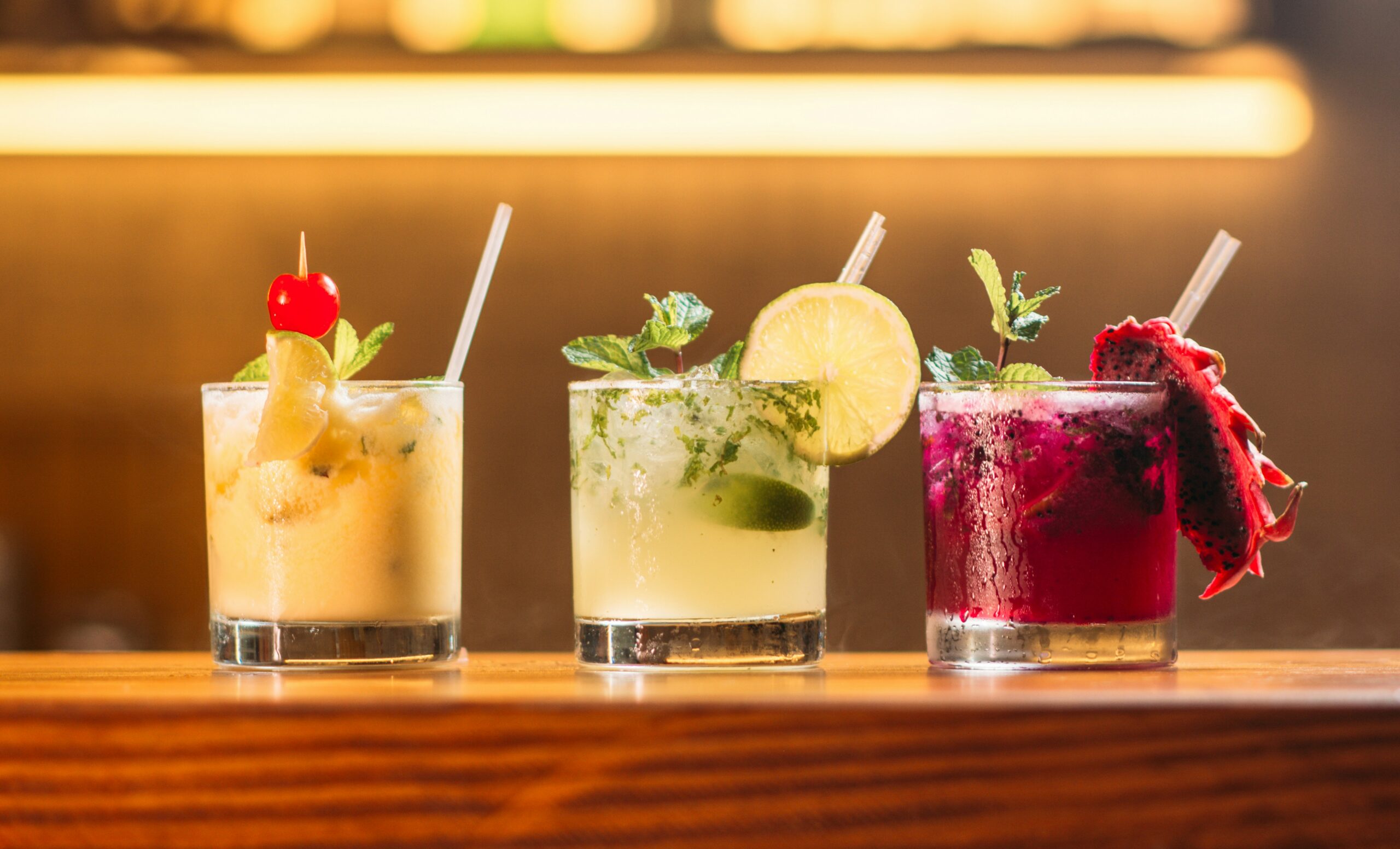 Three colorful cocktails on a wooden table top